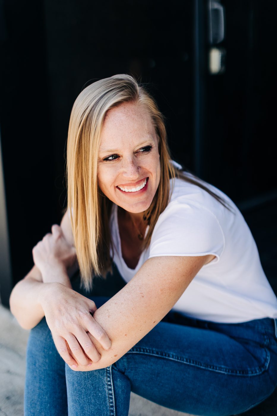 Christi Loucks sitting on a step in a white tee, laughing